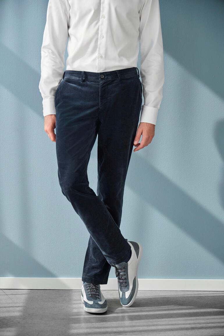 Man draagt een zwarte fluwelen broek, zijaanzicht voor een blauwe achtergrond.