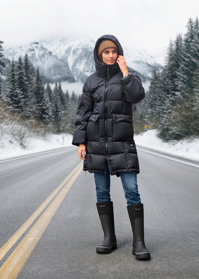 Tretorn rubberlaarzen voor de winter Vrouw in Taion donsparka met capuchon staand in een winterlandschap.