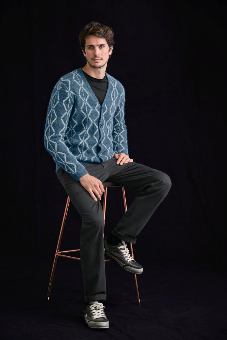 zwart Man zit op een barkruk in een blauwe geborstelde alpaca cardigan met ruitpatroon.