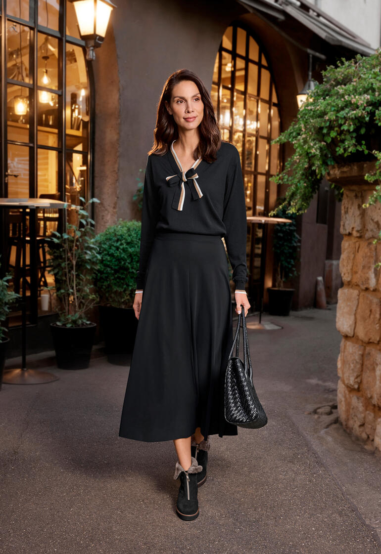 Vrouw in zwarte jurk met strikje op de stoep voor een café