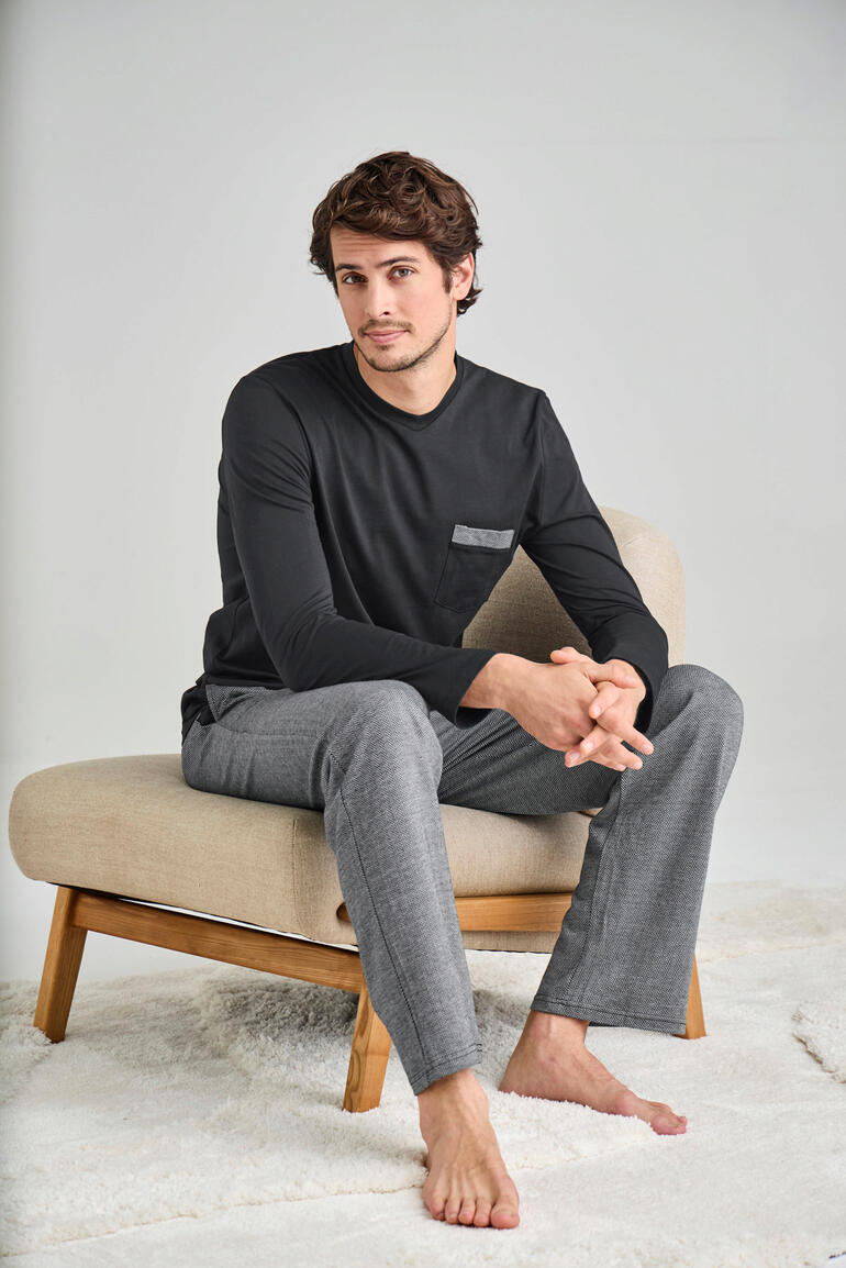 Lievelingspyjama lang Man zit op een stoel in zwart t-shirt met lange mouwen en grijze pyjamabroek.