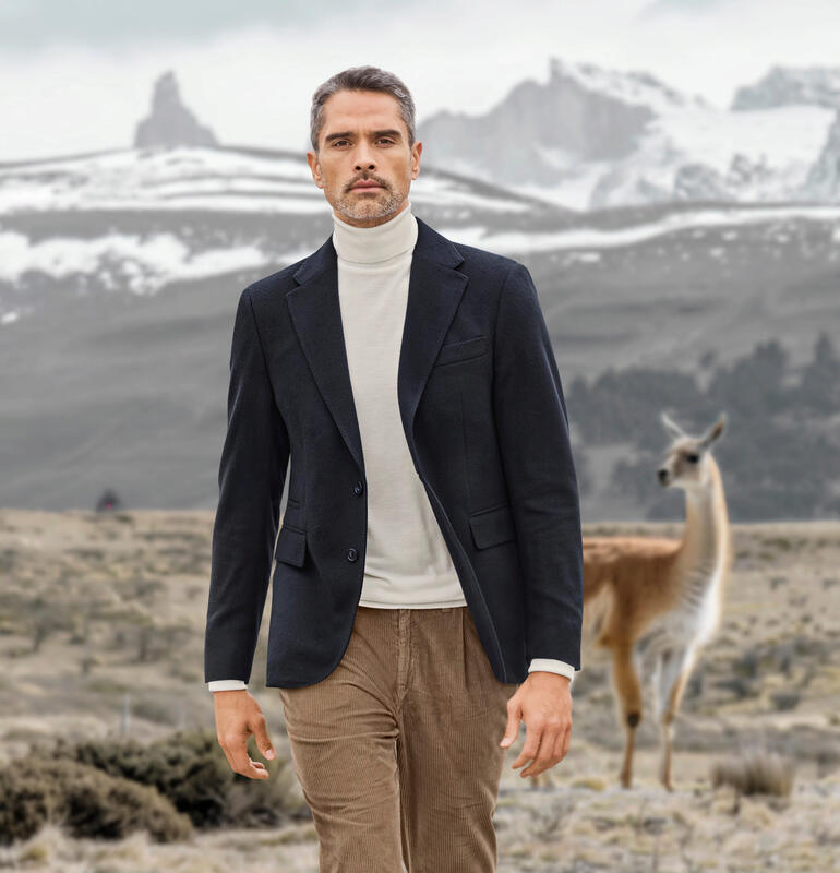 Blazer van vicuña Vicuña colbert in marineblauw, model loopt door landschap met een lama op de achtergrond.