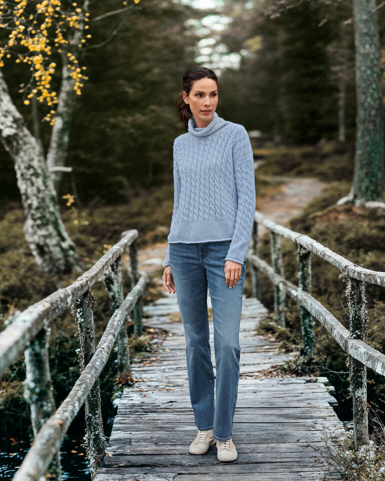 Vrouw in blauwe gebreide trui en spijkerbroek op houten brug in het bos