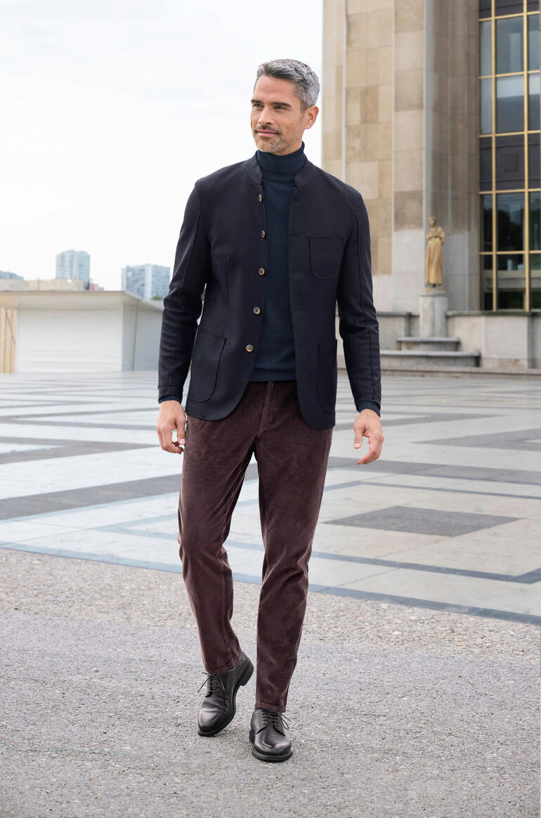 druif Man in casual janker en corduroy broek, terwijl hij voor een gebouw loopt.