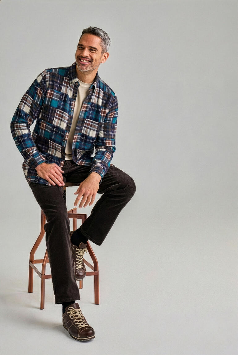 Man zit op een kruk en draagt een geruite flanellen shirt in blauw en bruin.