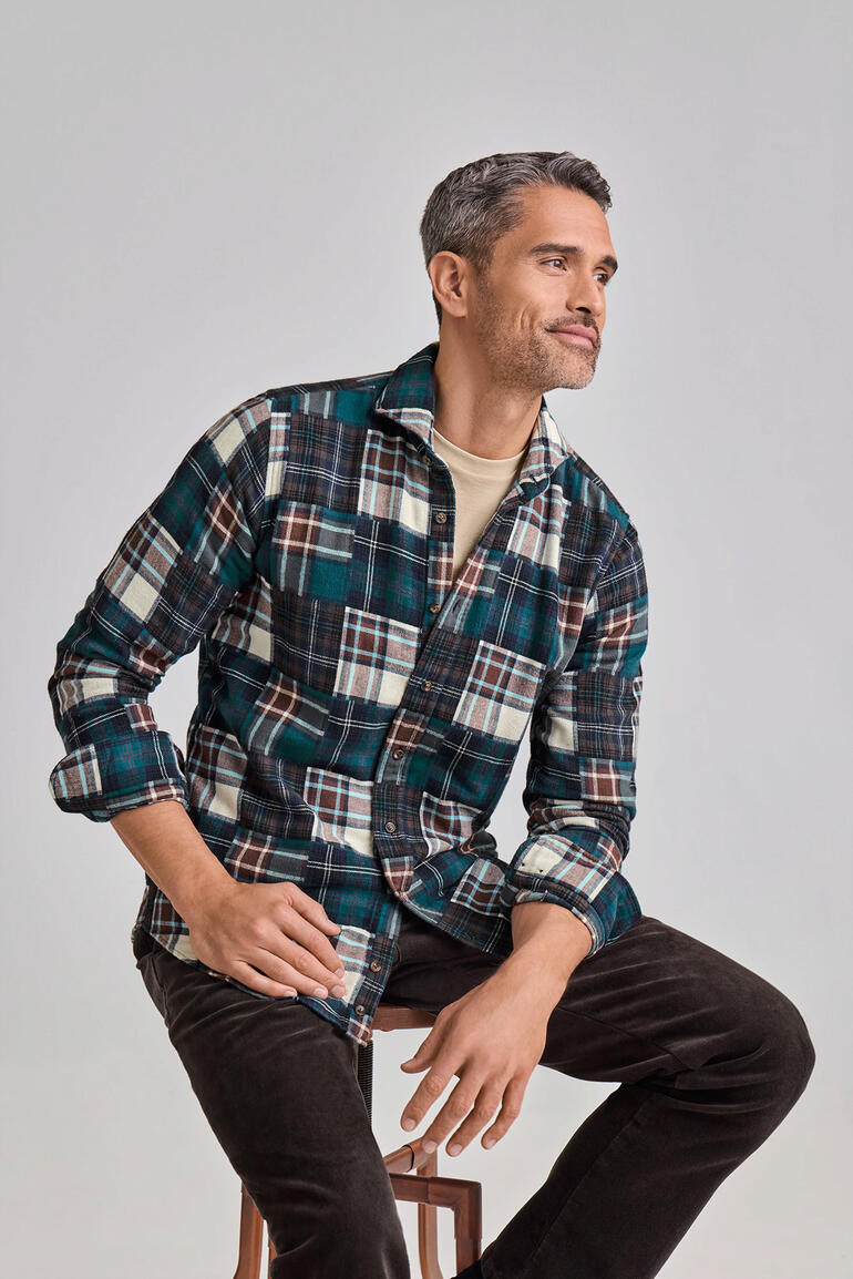 DU4 patchwork-overhemd van flanel Man draagt een DU4 patchwork flanellen overhemd met ruitjes, zittend op een kruk.