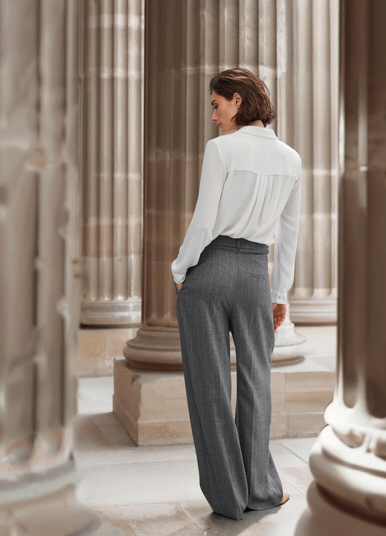 Vrouw van achteren in een elegante outfit, toont de gestreepte broek.
