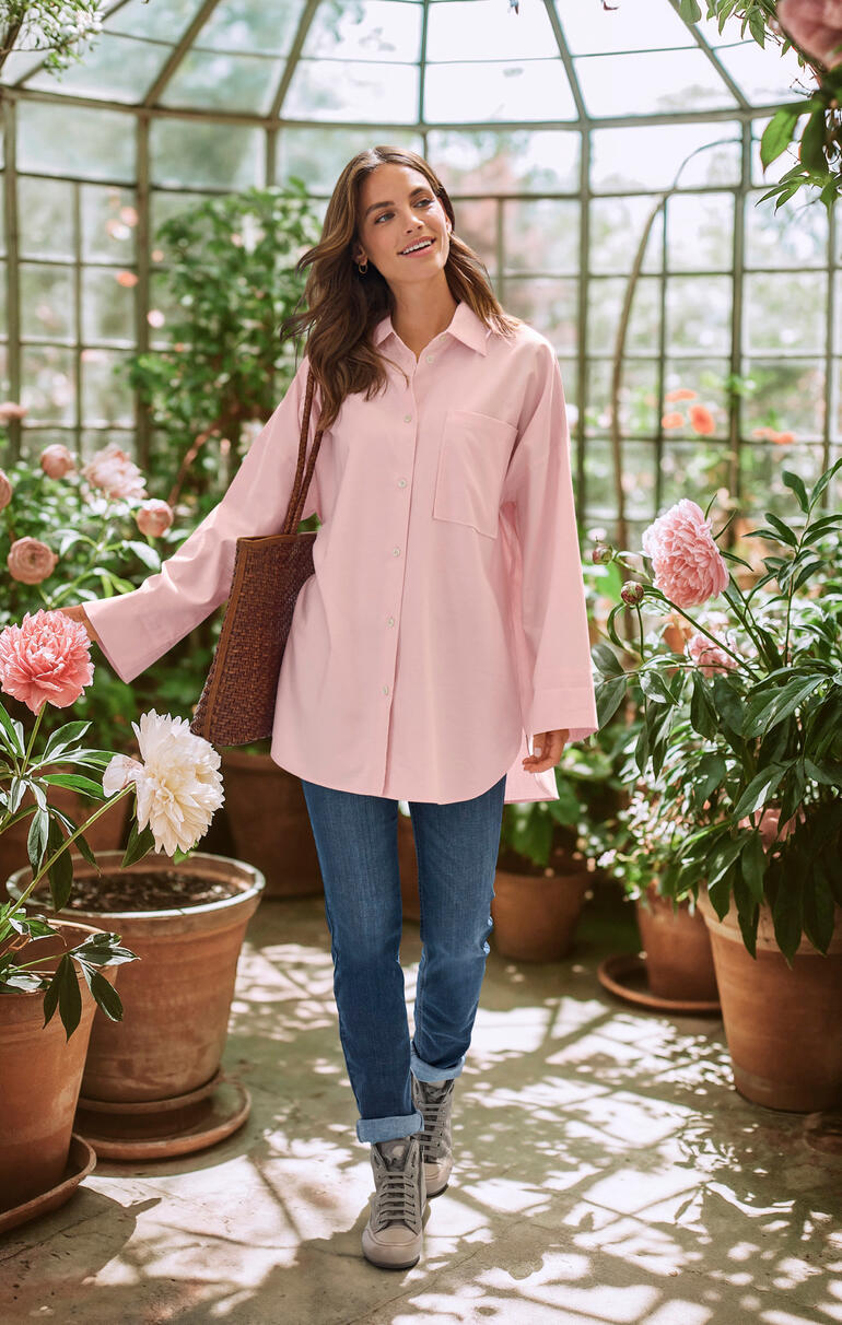 Oversized winterblouse Vrouw in een roze oversized winterblouse staat in een serre.