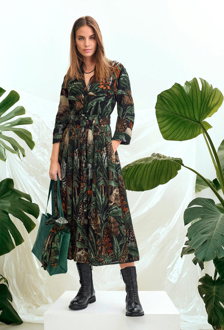 Samantha Sung Jungle jurk Vrouw in een lange wollen jurk met junglepatroon, staande voor tropische planten.