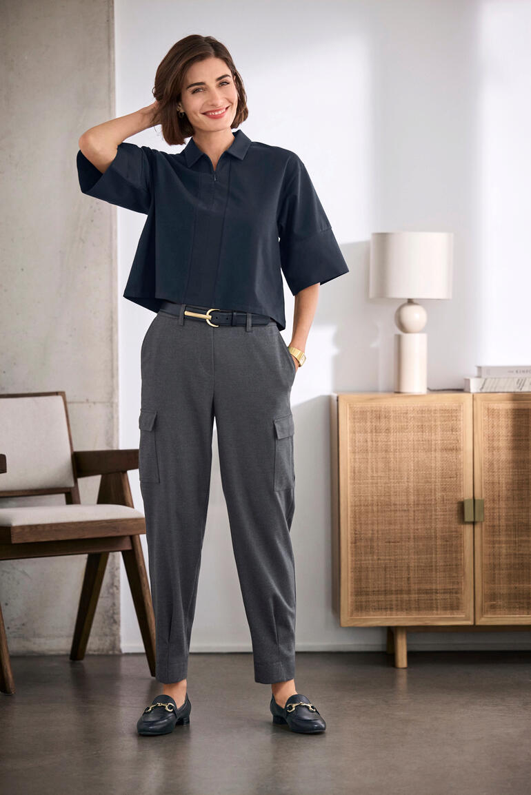 Vrouw in een Boxy oversize blouse, gecombineerd met elegante broeken in een modern interieur.