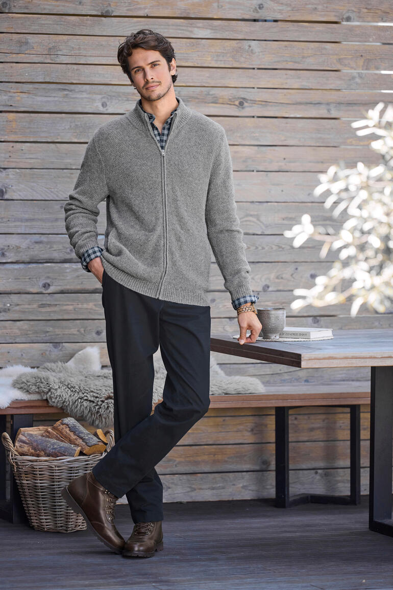 Man in een grijze alpaca klimaat cardigan voor een houten wand