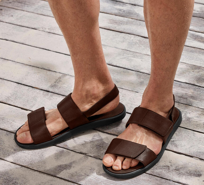 Bruine leren sandaal met twee banden op een voet op een houten vloer.