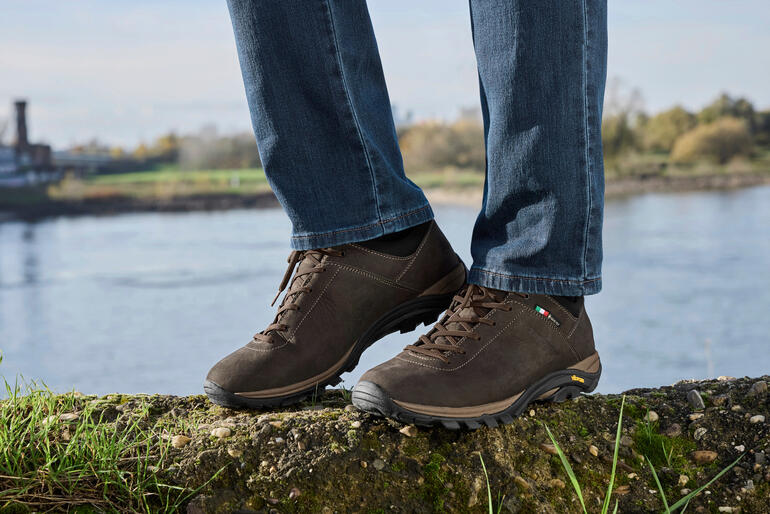heren, donkerbruin Bruine Zamberlan sneakers Commute GTX op een rots bij een waterlichaam.