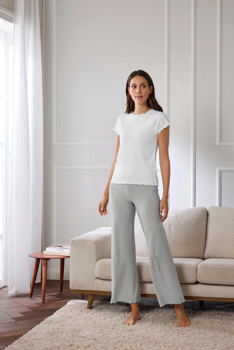 Vrouw staat in een grijze modal ribbed pyjama en een wit T-shirt voor een bank