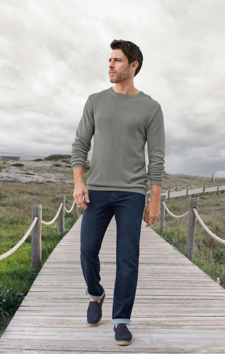 Man in een grijze Ivanhoe Tencel-Piqué-trui en jeans op een houten loopbrug.