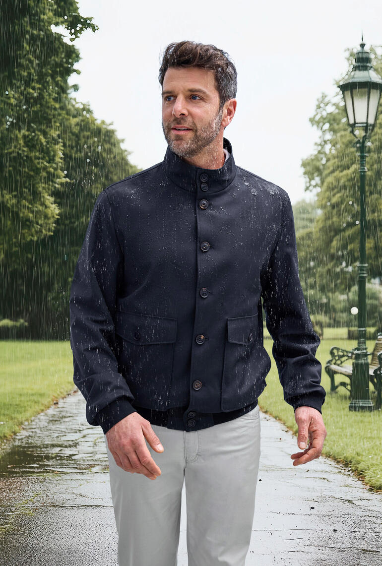 Dichtbij een man in Storm-System®-blouson die de regen absorbeert met een blauwe achtergrond.