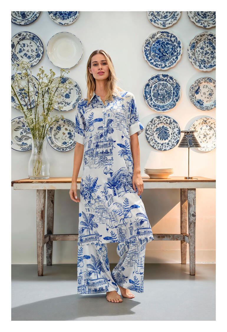 blousejurkje en broek met wijde pijpen Vrouw in Esisto zijden stretchcombinatie staat voor een muur met blauwe borden.
