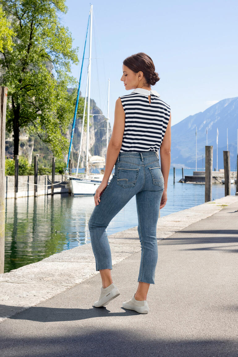 Silver Suki straight jeans Vrouw in gestreept top en jeans op een trottoir bij het water.