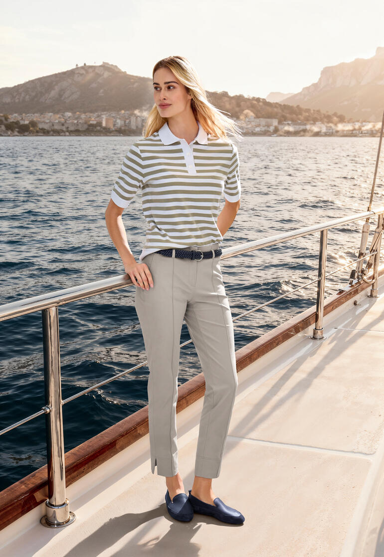 Vrouw draagt een beige boxy poloshirt met strepen, poserend aan de oever van een bergmeer.