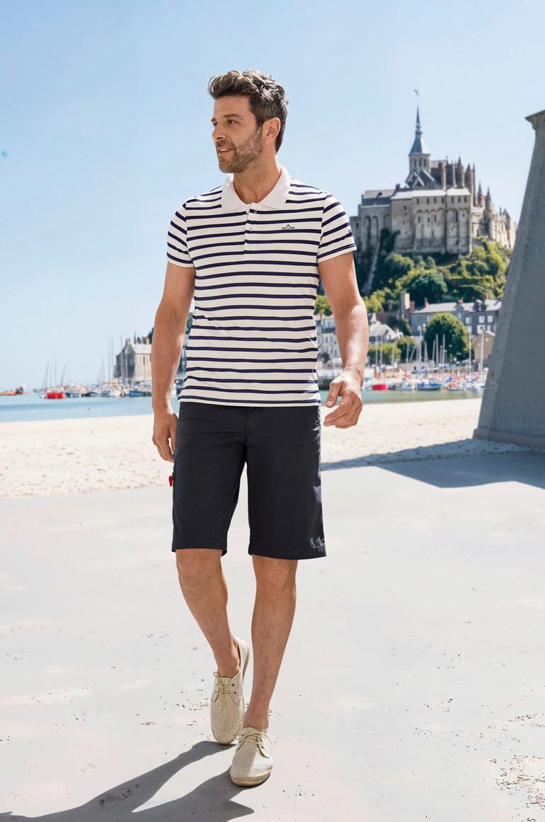 Saint James Bretons poloshirt Man in gestreept Saint James Bretagne Poloshirt, wandelend op het strand.