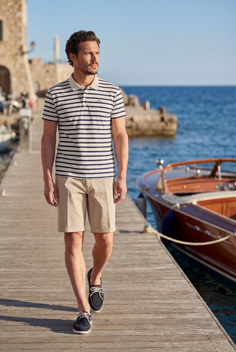 Man in gestreept poloshirt en shorts aan de haven.