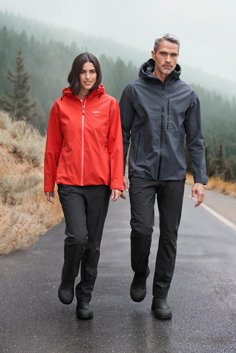 Mannen in waterdichte jas en broek bij mistig weer.