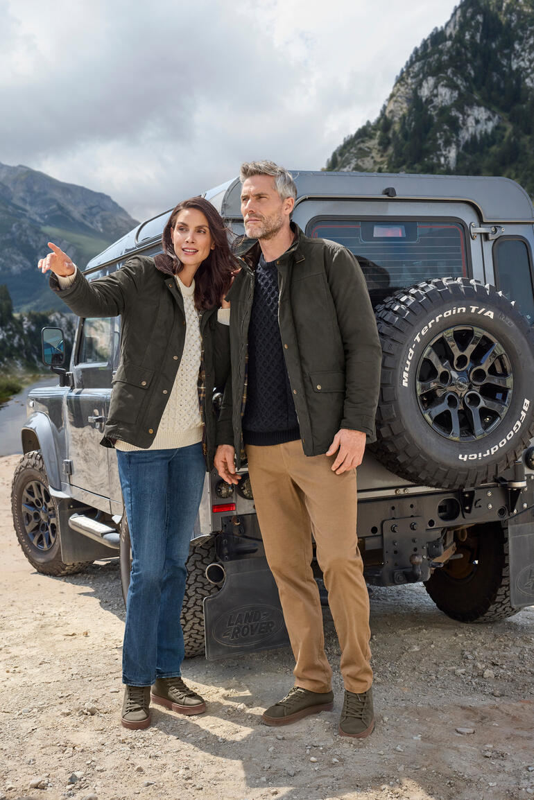 Koppel in outdoorjacks staat voor een terreinwagen in een natuurlijke omgeving.