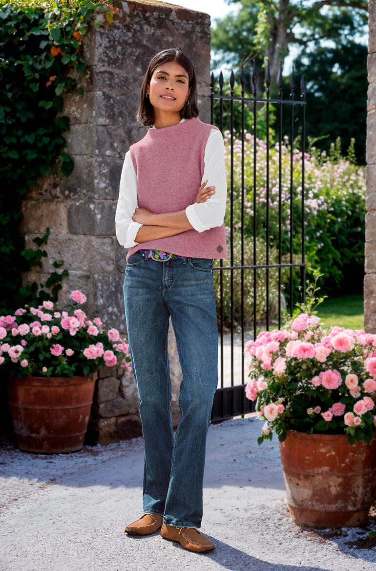 roze Vrouw in een roze wool vest over een wit longsleeve, staat aan een bloeiende poort.