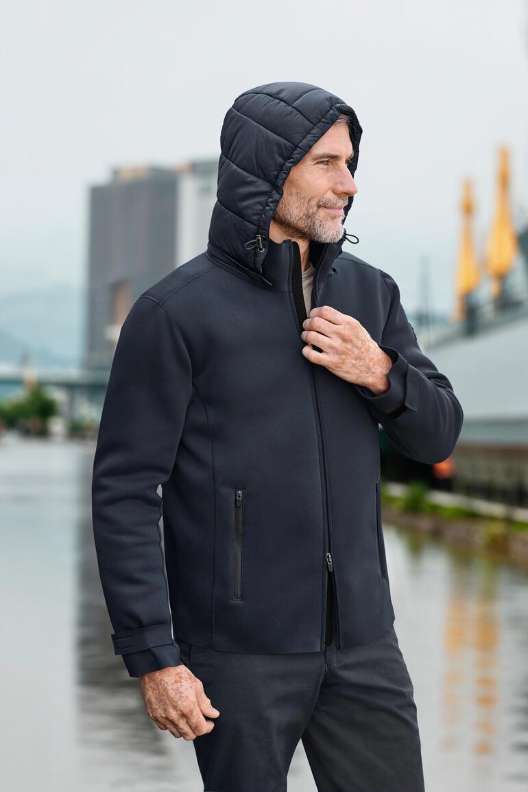 Man in een neopreen buitenjas met capuchon staat buiten.