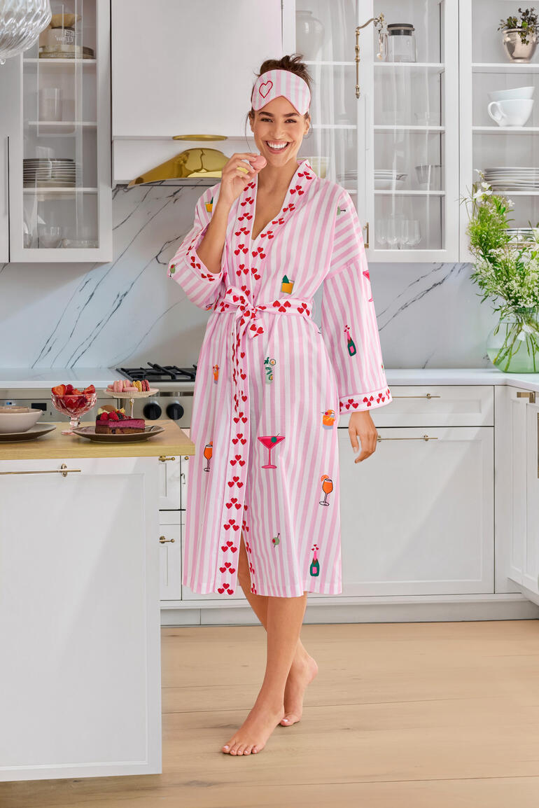 Nimo With Love sleepover-set Vrouw draagt een gestreepte ochtendjas met kleurrijke motieven in een moderne keuken.