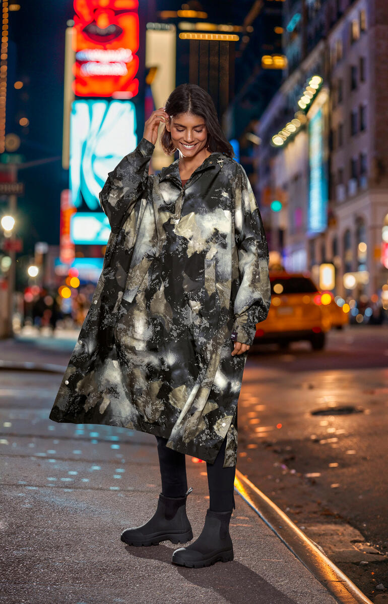 Ilse Jacobsen design-regenponcho Vrouw draagt een gemêleerde regenponcho in een stad 's nachts.