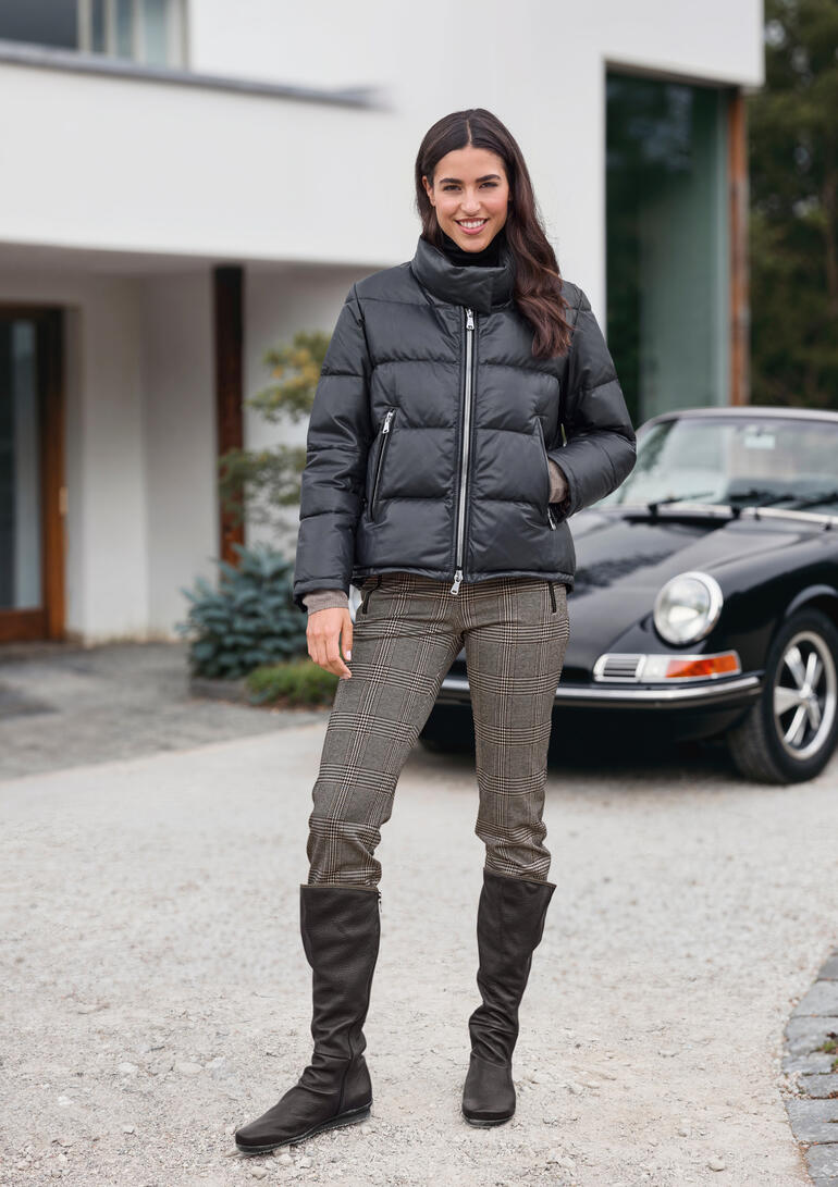 Vrouw in een zwarte donsjas staat voor een auto op een pad.