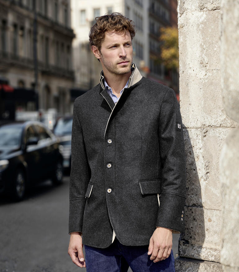 Man in merino lodenjas staat tegen een muur in de stad