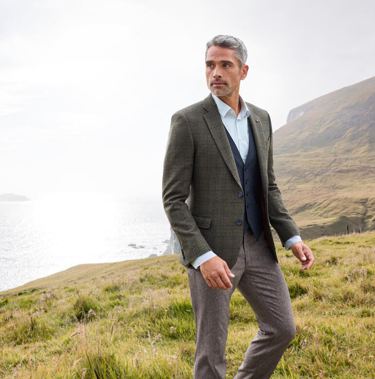 Man in een geruite blazer in een heuvelachtig landschap.
