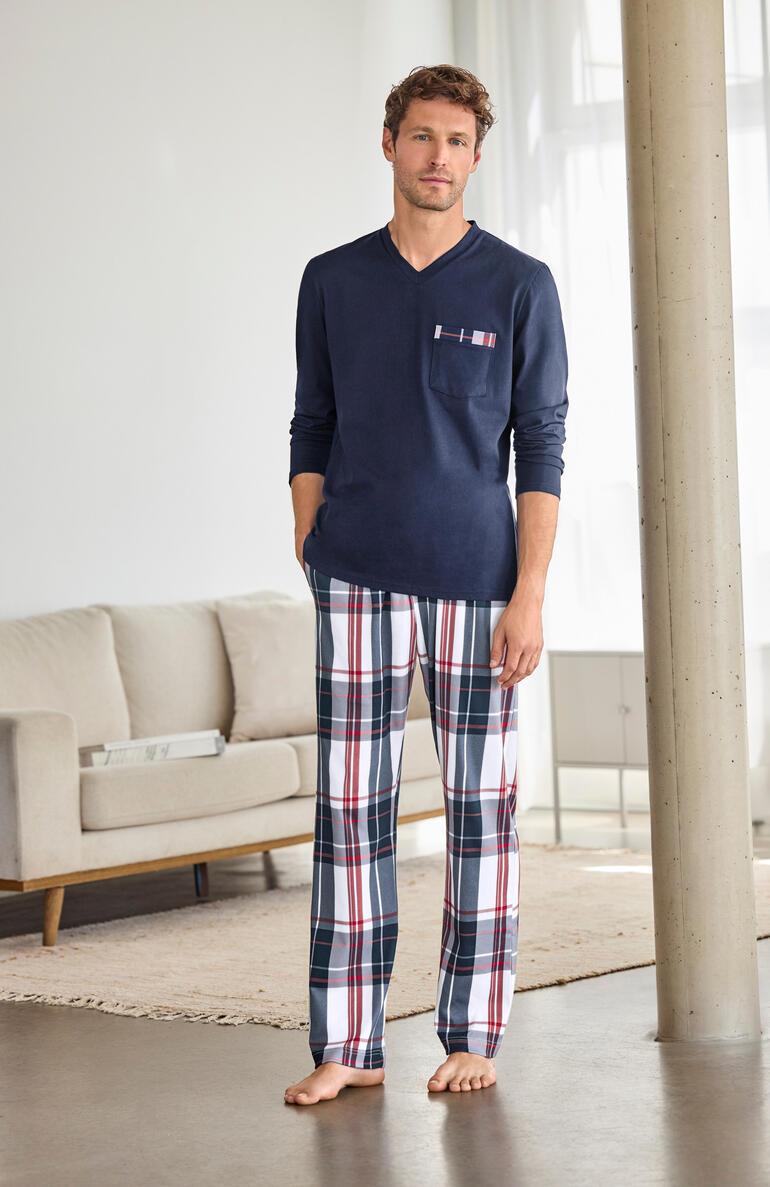 Man in een blauw geruit pyjama met broek staat in een woonkamer.