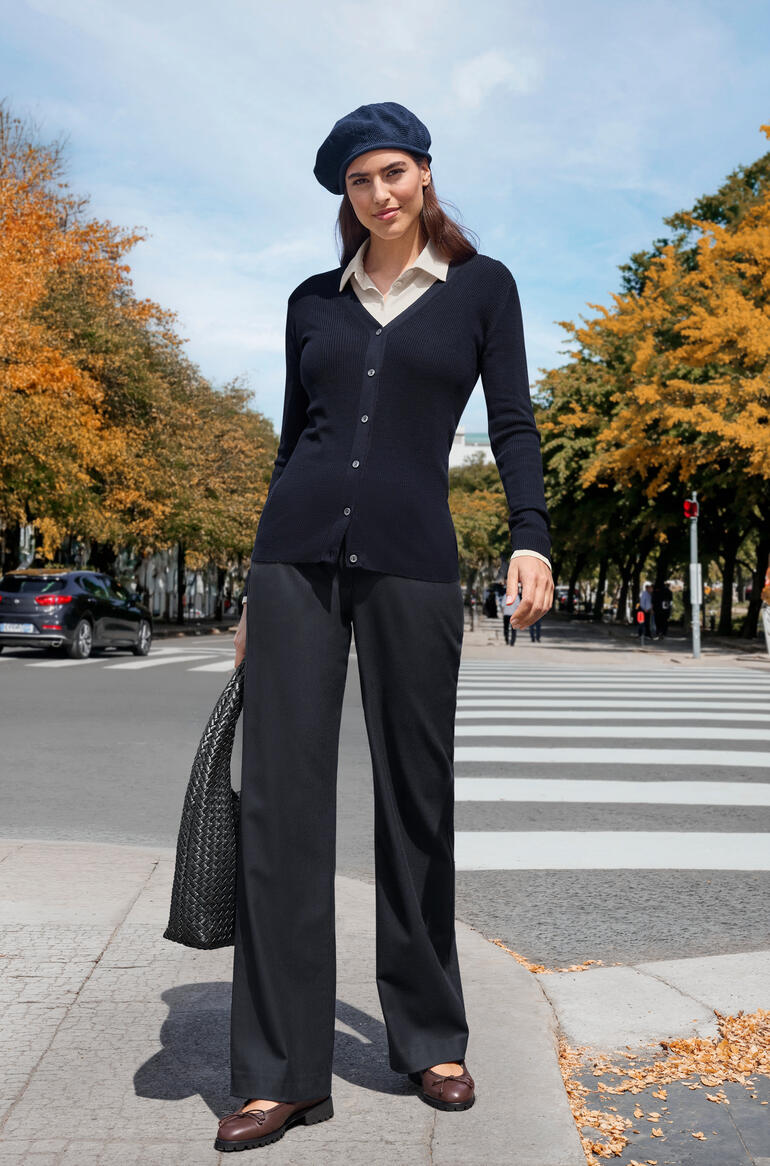 Vrouw in donkerblauwe vest en zwarte broek in een herfstachtige omgeving.