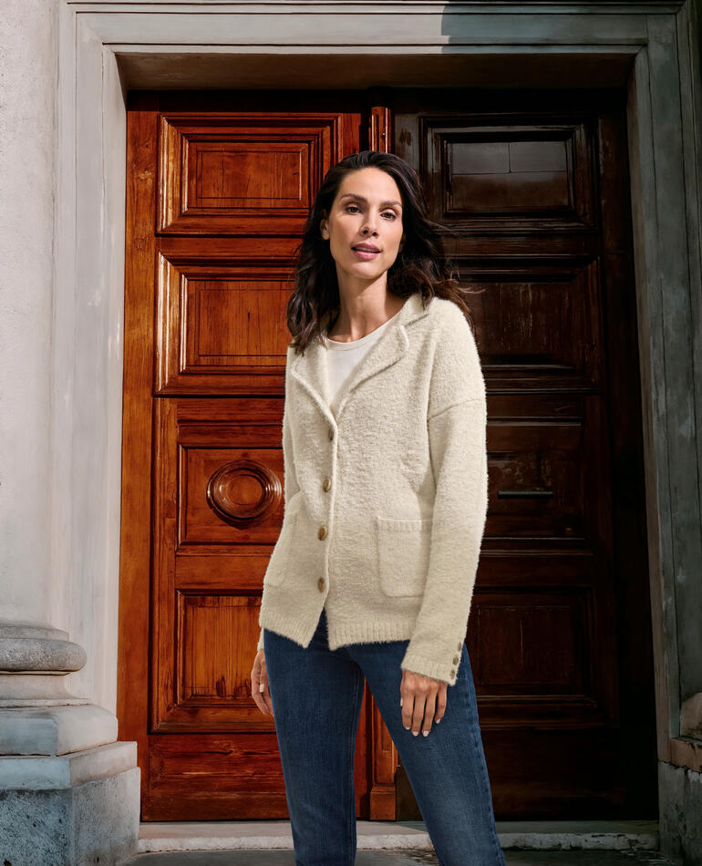 Vrouw in ecru gebreide blazer staat voor een historische deur.