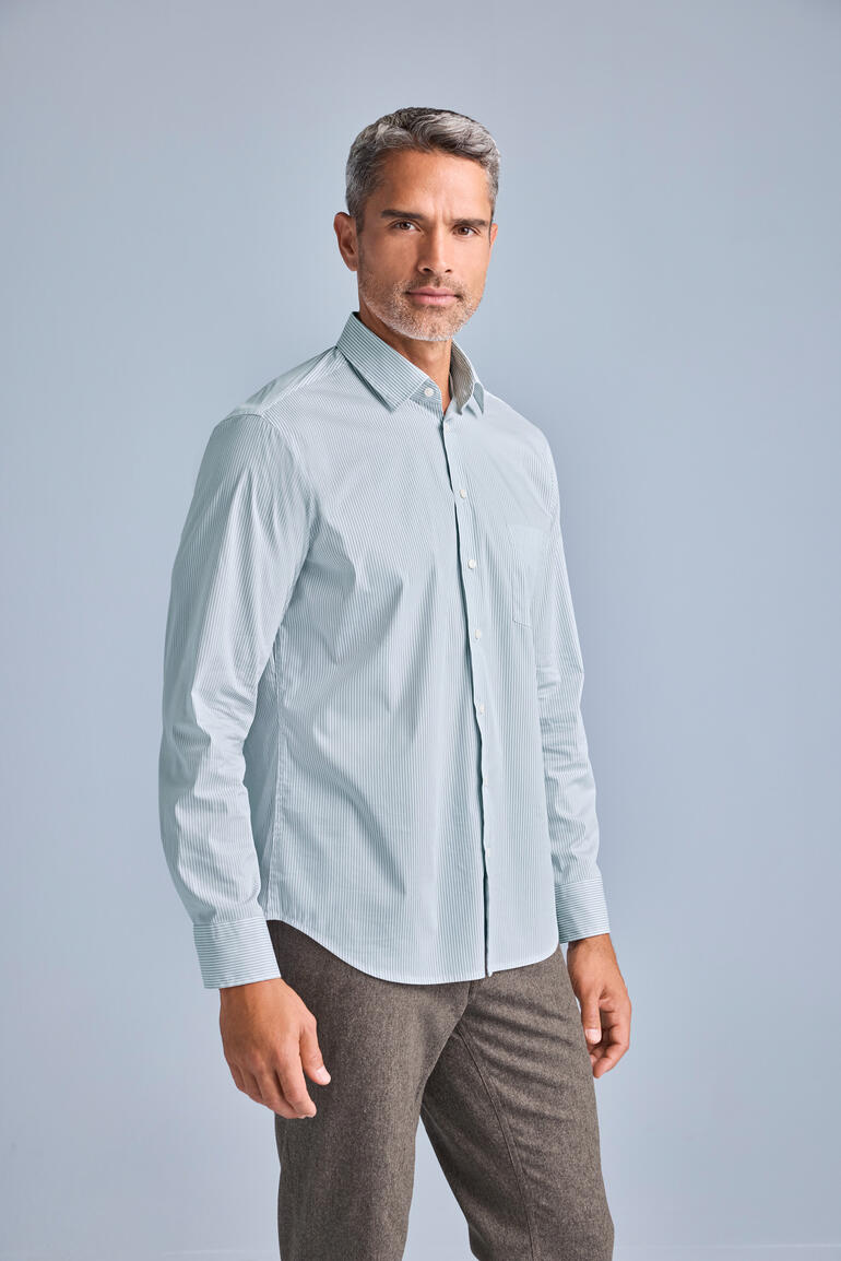 Man in een lichtblauw merino-zijden overhemd staat in een studio.