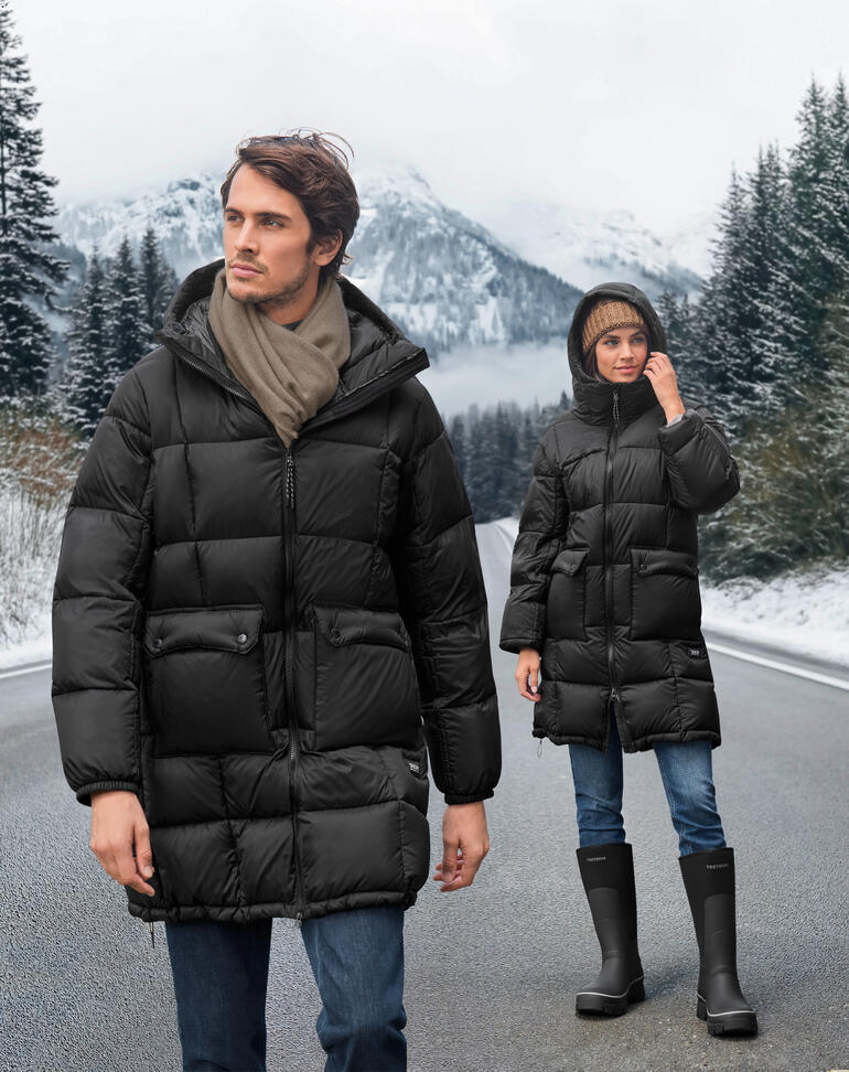 Twee personen in zwarte dons parka op een winterse weg met bergen op de achtergrond.