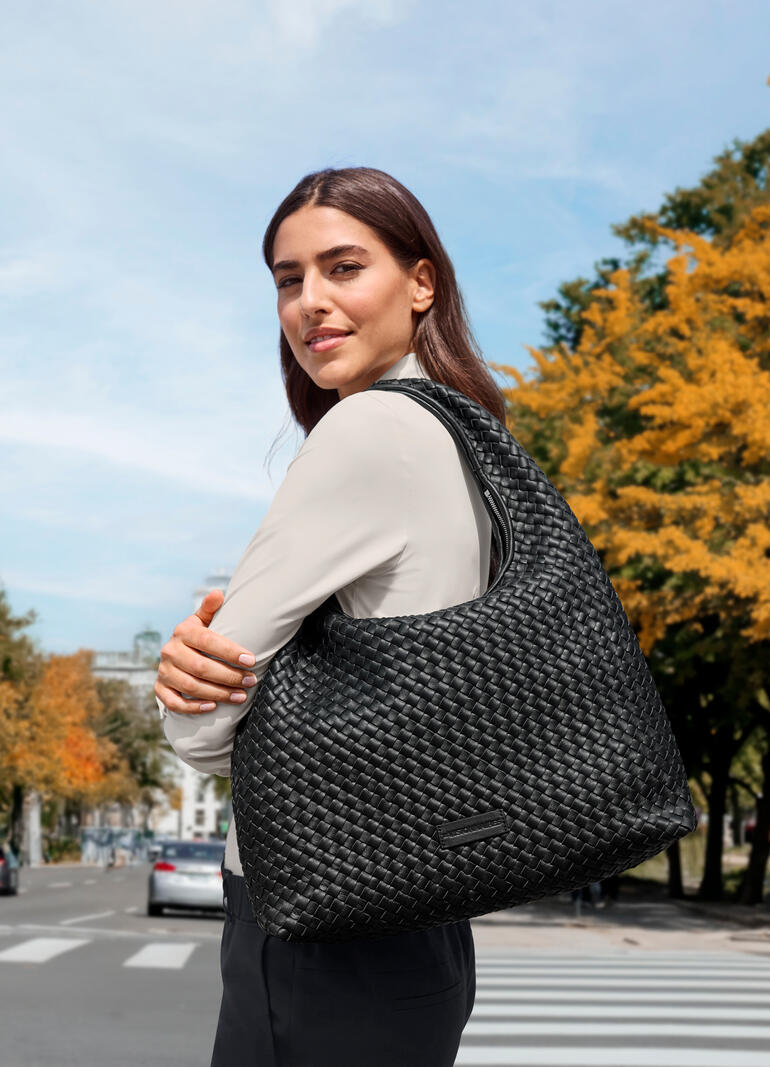 Vrouw draagt zwarte Hobo vlecht tas op een drukke straat in de herfst.