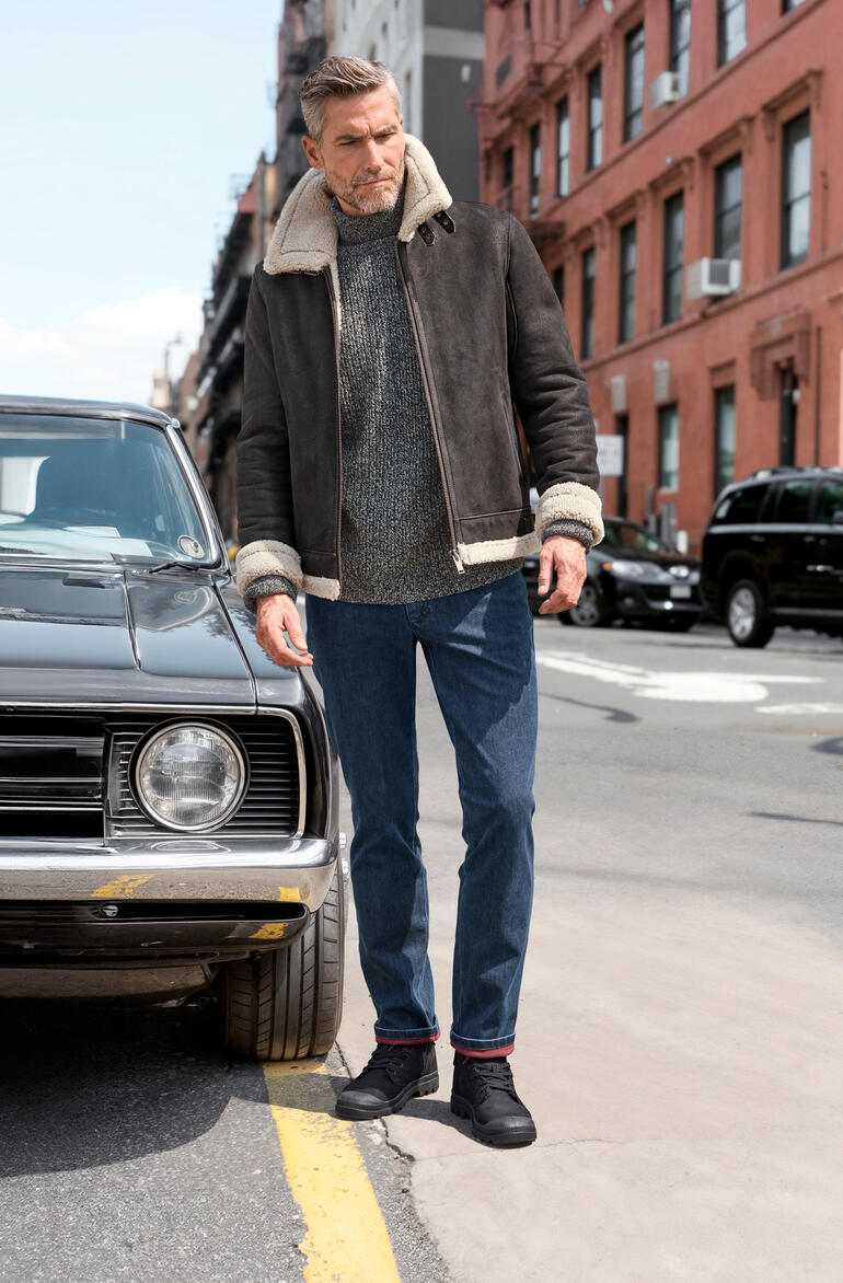 Man in een bruine lammy-pilotenjack en grijze trui voor een oldtimer.