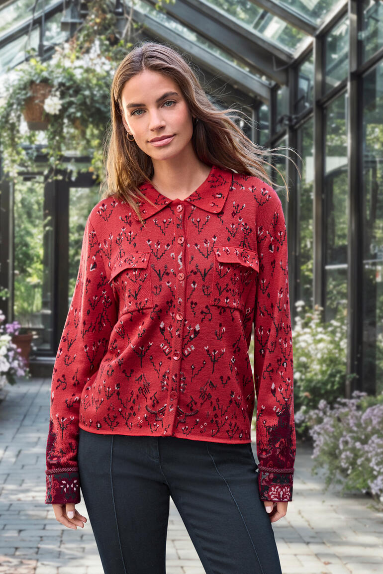 Vrouw in een rode jacquard gebreide blouse met bloemmotief in een serre.