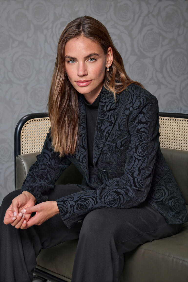 Flanellen blazer met rozendessin Vrouw in gebloemde blazer zit in een stijlvolle ruimte.