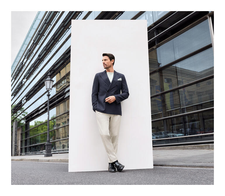Man in een blauwe blazer en beige broek poseert op de stoep.