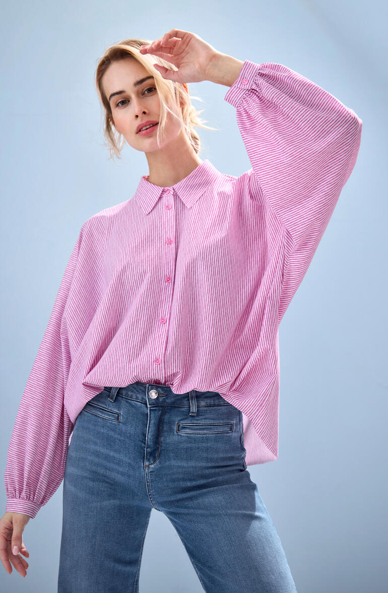 Vrouw in een roze gestreepte blouse met losse mouwen.