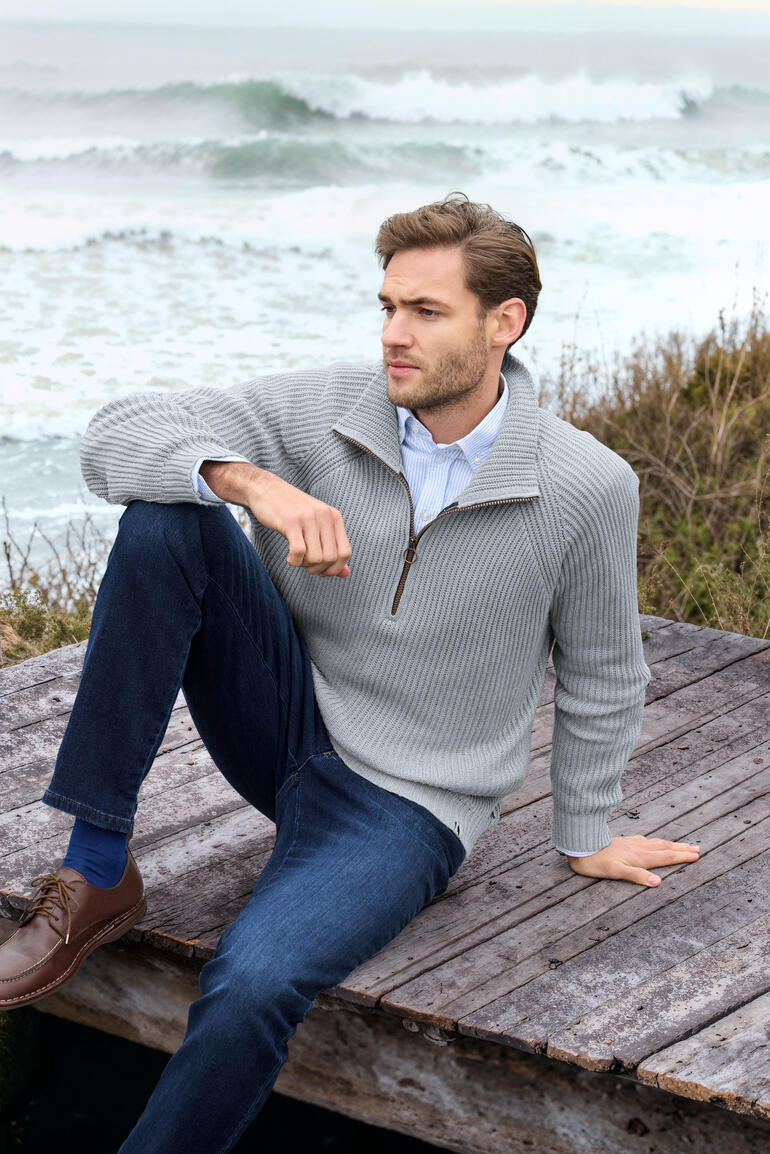 Man in ribbeltrui zit op het strand en kijkt naar de zee.
