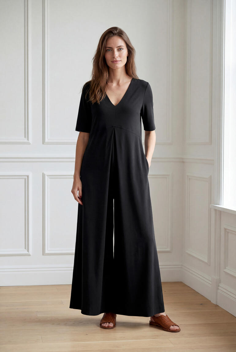 Vrouw in een zwarte jersey jumpsuit staat glimlachend in een lichte ruimte.