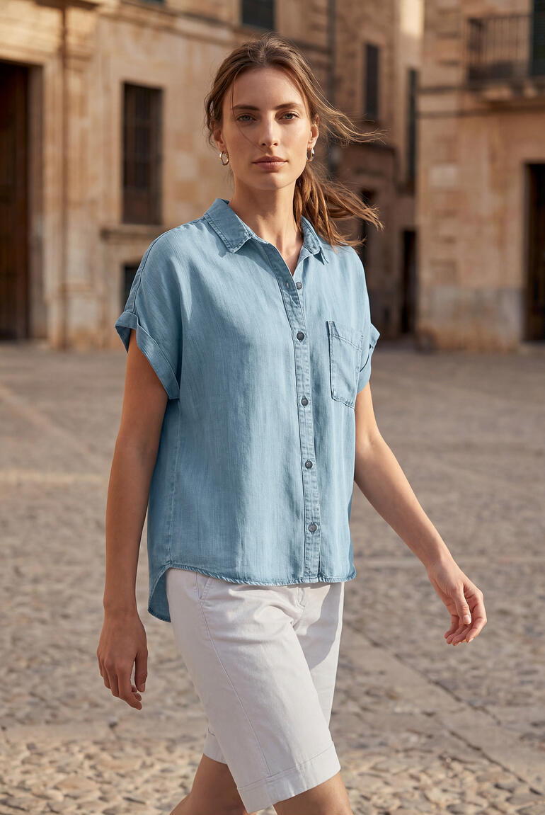 Vrouw in een blauwe korte-erm foamjeansblouse loopt zelfverzekerd op een straat.