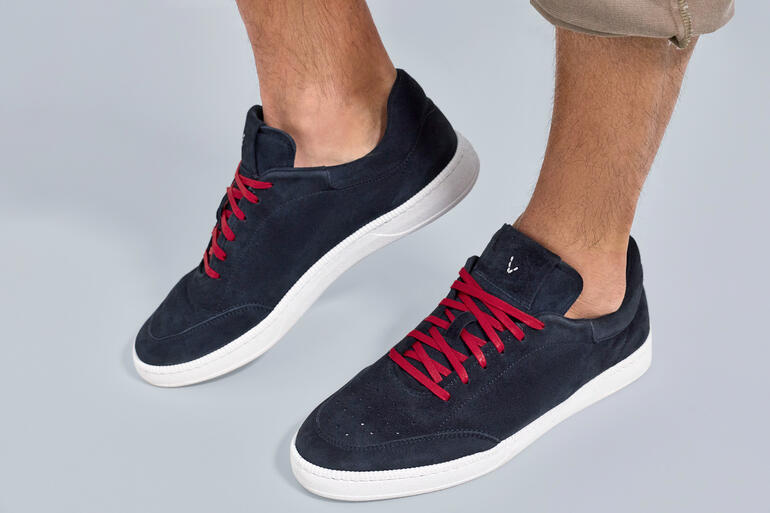 Marineblauwe zomersneakers met rode veters, staan op een grijze ondergrond.