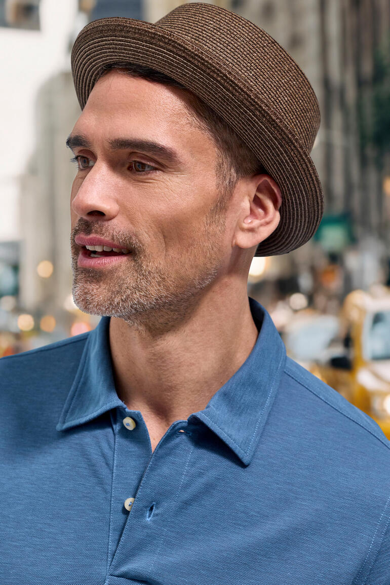 Man met een bruine Pork Pie hoed en een blauwe poloshirt.